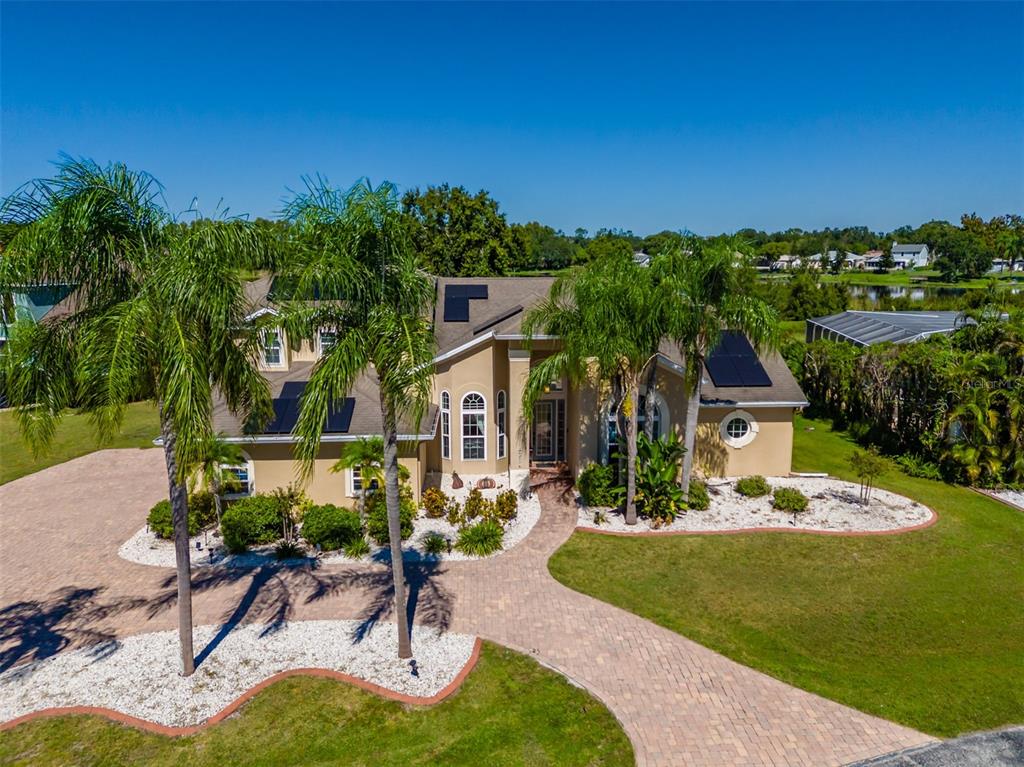 An aerial view of a tan two-story house with solar panels and a paved driveway — 2327 CAMP INDIANHEAD ROAD, LAND O LAKES, FL