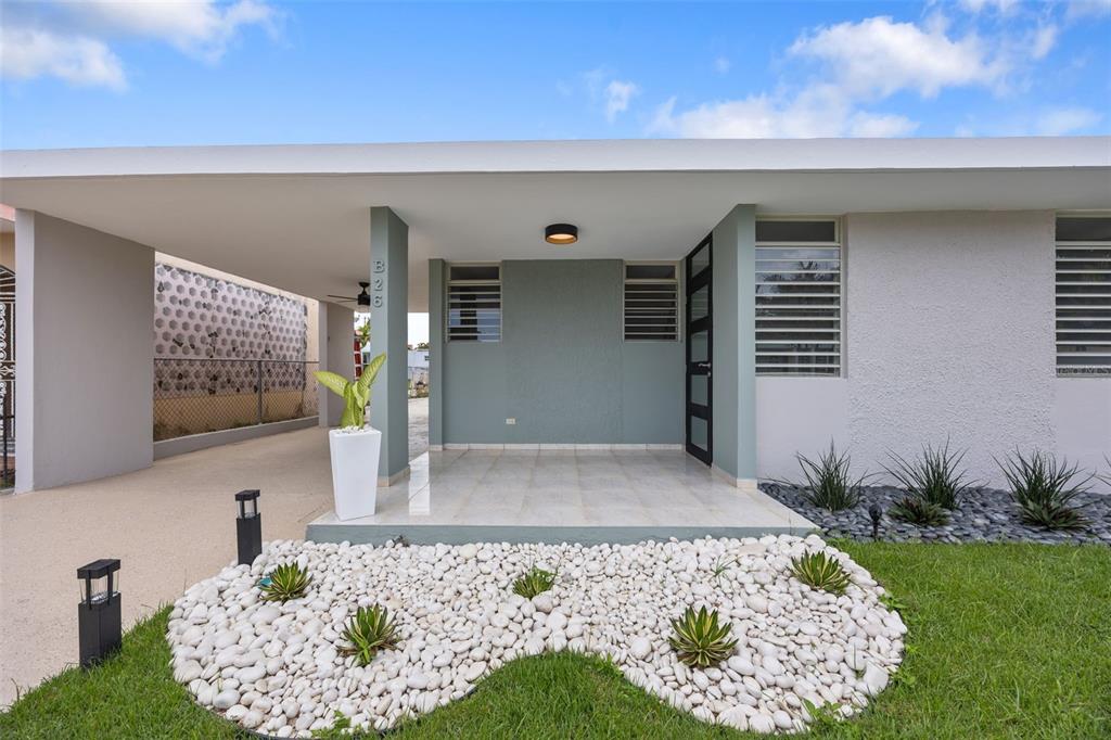 The exterior of a modern house features a covered porch, white stone landscaping, and a carport — CASA SUAVE CALLE 4 UNIT B-26, AGUADA, PR
