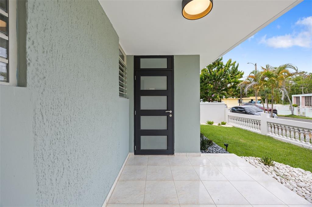 A modern front door with five frosted glass panels sits on a tiled porch — CASA SUAVE CALLE 4 UNIT B-26, AGUADA, PR