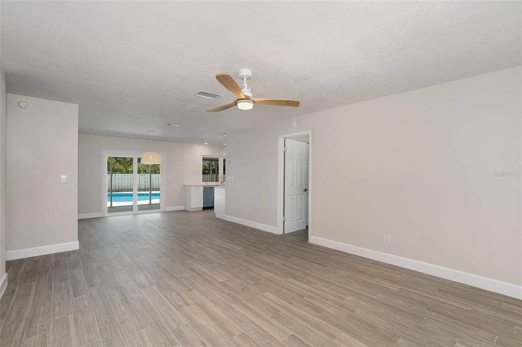 An open-concept living area features light wood-look tile flooring, a ceiling fan, and sliding doors — 125 MATANZAS ROAD, MELBOURNE BEACH, FL