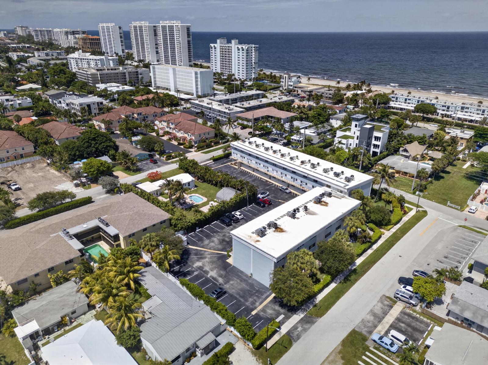 An aerial view shows a multi-story apartment complex with parking lots near a coastal beach — 505 NE 20th Avenue # 209, Deerfield Beach FL 33441, DEERFIELD BEACH, FL