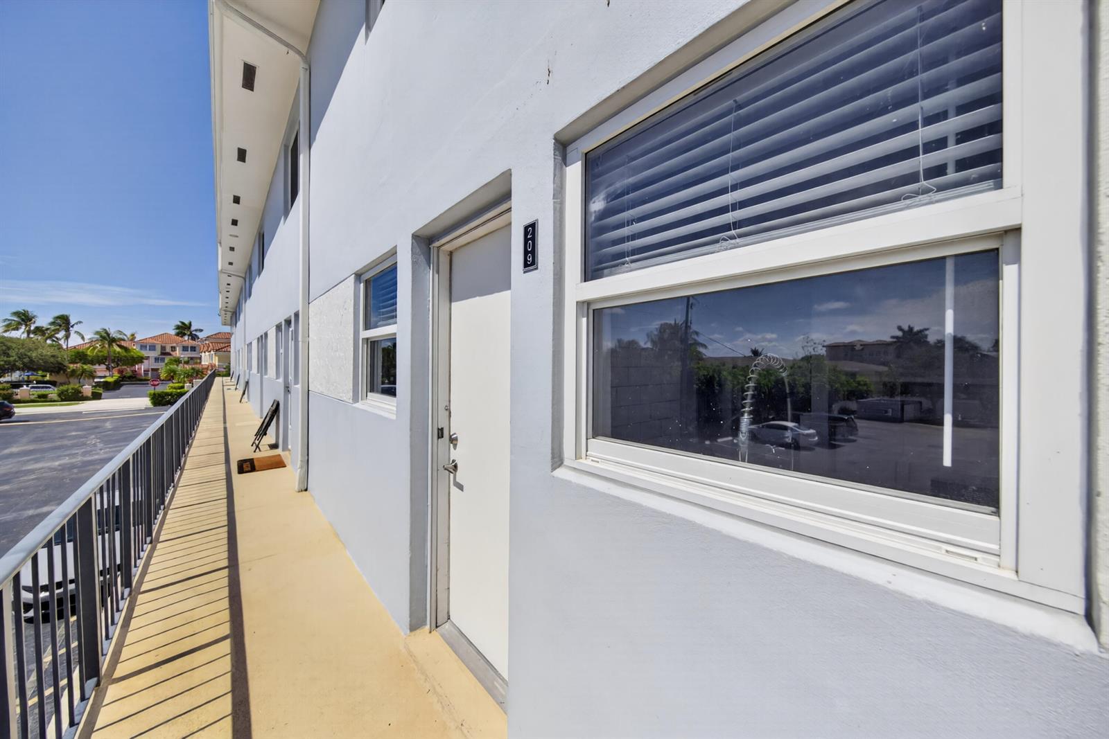 An exterior view of a building walkway featuring a white door labeled 209 and windows — 505 NE 20th Avenue # 209, Deerfield Beach FL 33441, DEERFIELD BEACH, FL