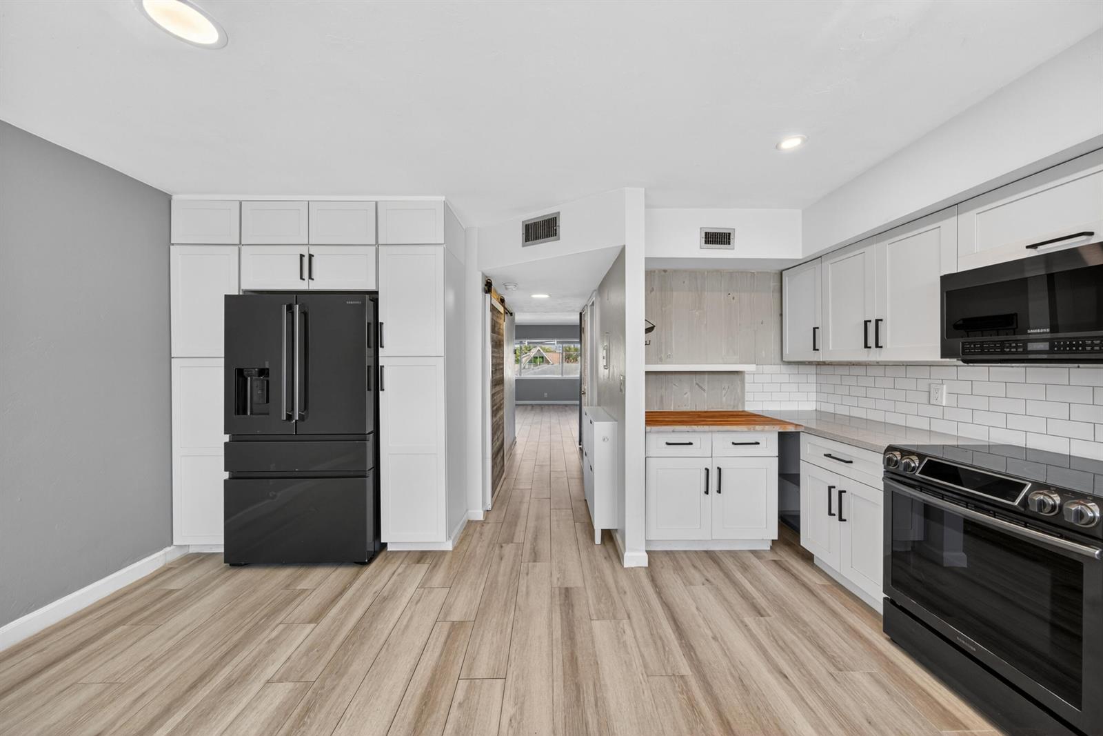 A kitchen features white cabinetry, a black refrigerator, a black range, and wood-look flooring — 505 NE 20th Avenue # 209, Deerfield Beach FL 33441, DEERFIELD BEACH, FL