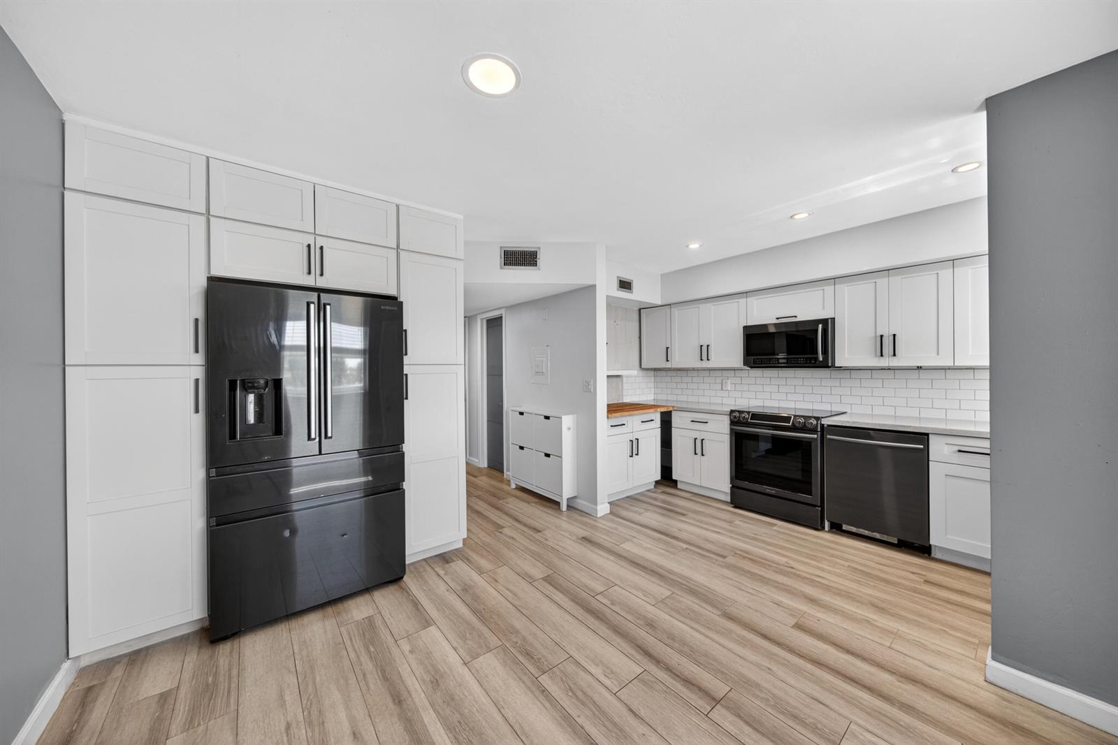 A modern kitchen features white cabinetry, black appliances, and light wood-look flooring — 505 NE 20th Avenue # 209, Deerfield Beach FL 33441, DEERFIELD BEACH, FL
