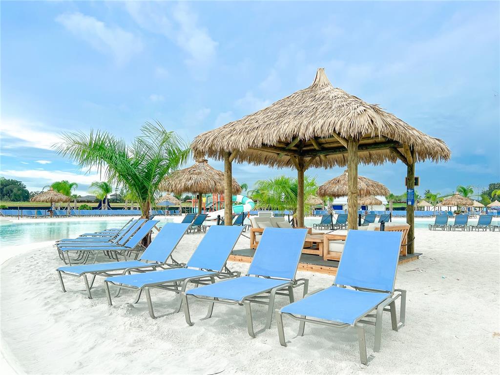 A sandy beach area features blue lounge chairs under a thatched-roof tiki hut — 31665 OCEAN BREEZE DRIVE, SAN ANTONIO, FL