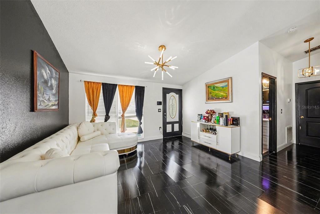 A living room features a white tufted sectional, black flooring, and a modern gold chandelier — 10119 CHIMNEY HILL COURT, TAMPA, FL