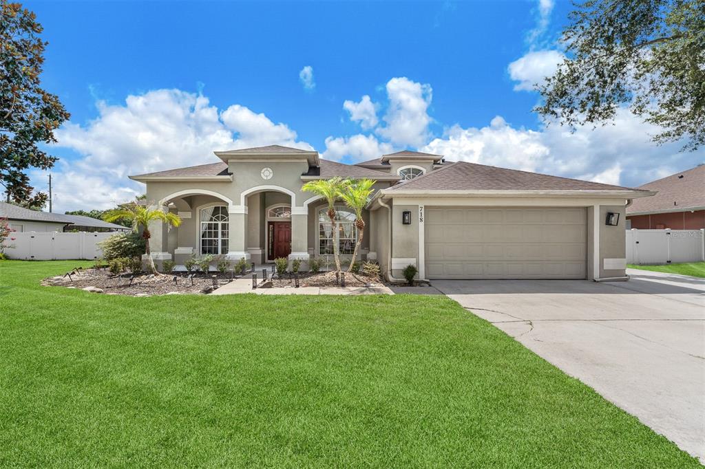 A single-story house with a beige stucco exterior, a two-car garage, and a landscaped lawn — 718 LITTLE HAMPTON LANE, GOTHA, FL