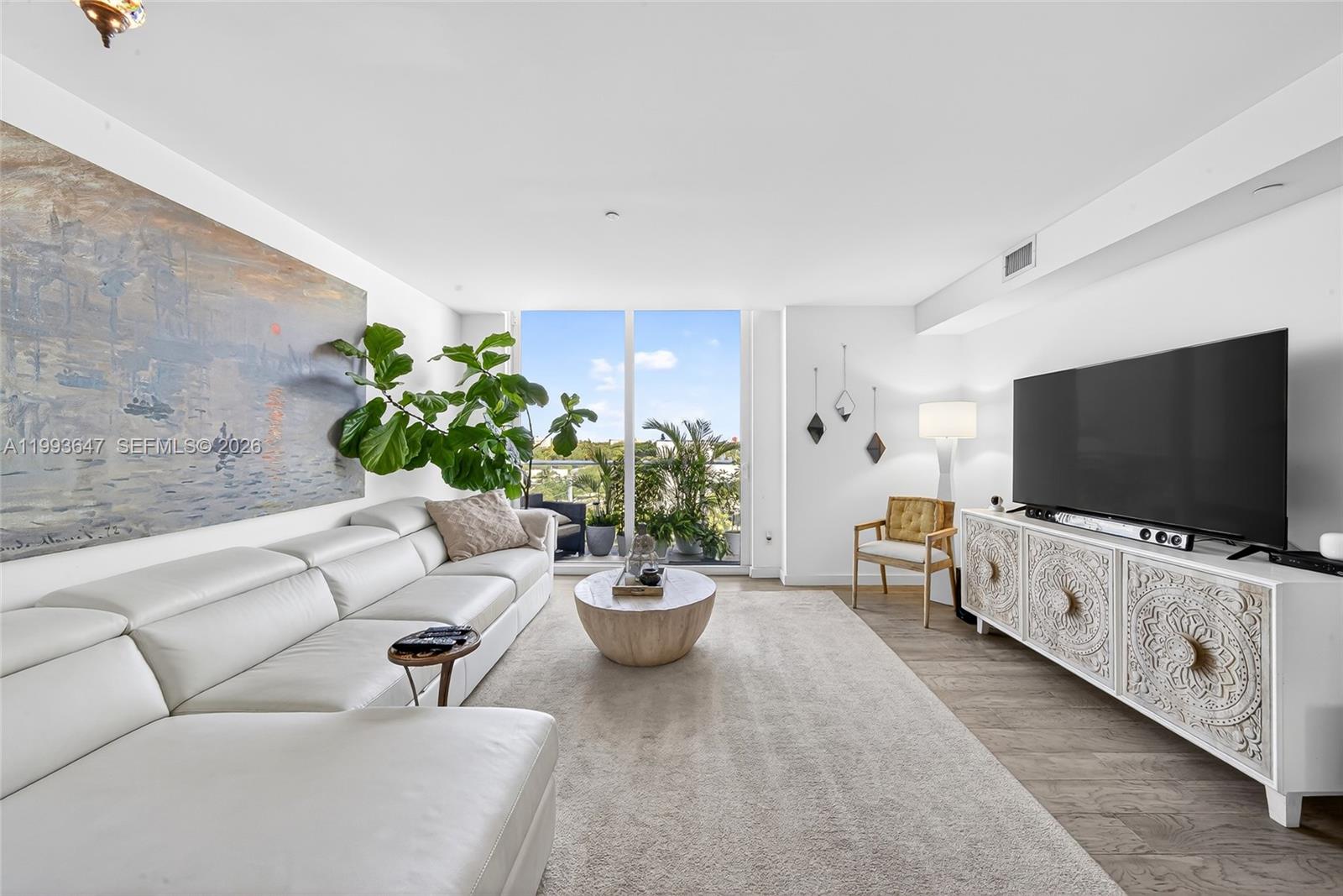 A modern living room features a white sectional sofa, a carved wooden media console, and floor-to-ceiling windows — 4250 Biscayne Blvd # 609, Miami FL 33137, MIAMI, FL