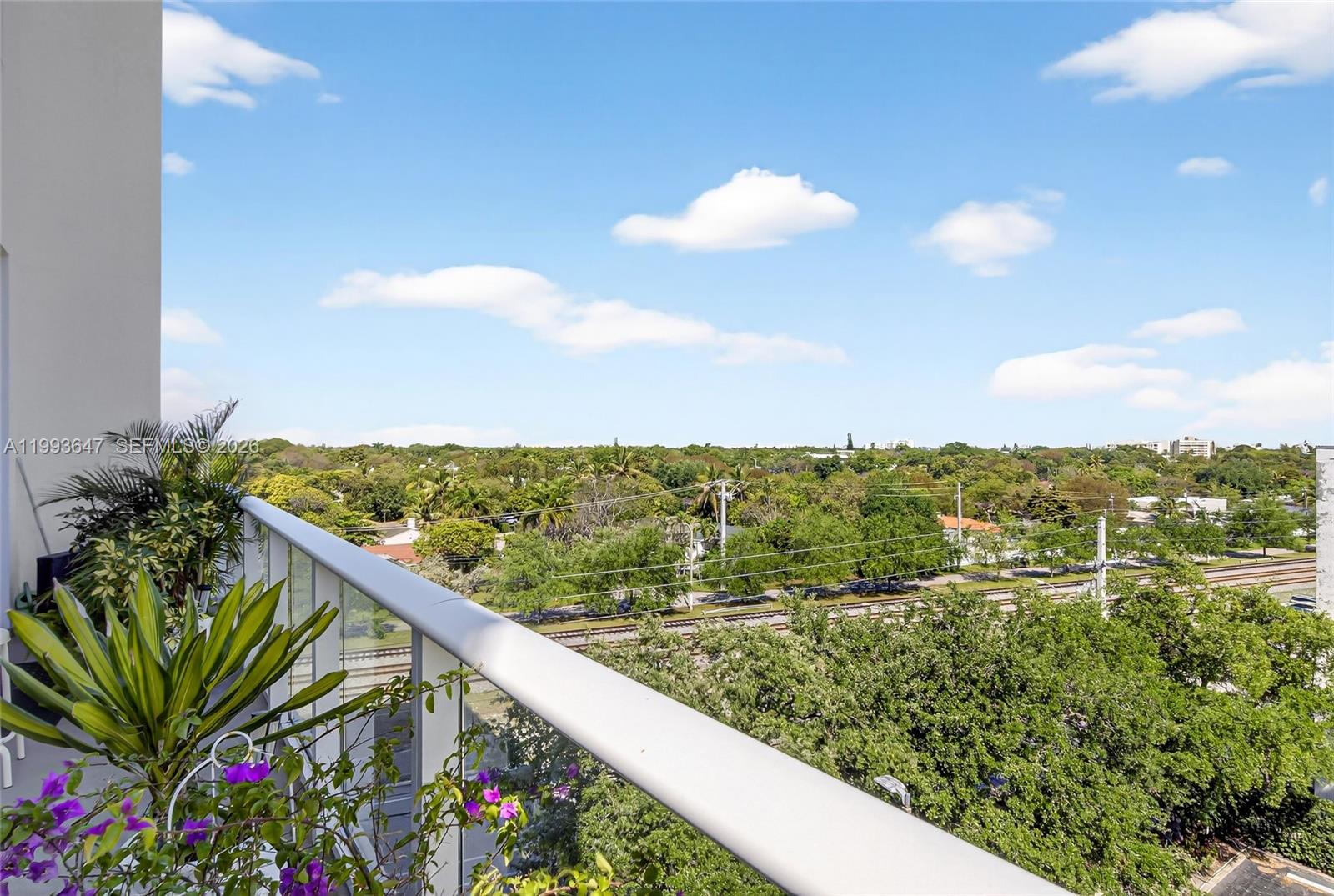A balcony view overlooks a lush green landscape, railroad tracks, and a clear blue sky — 4250 Biscayne Blvd # 609, Miami FL 33137, MIAMI, FL