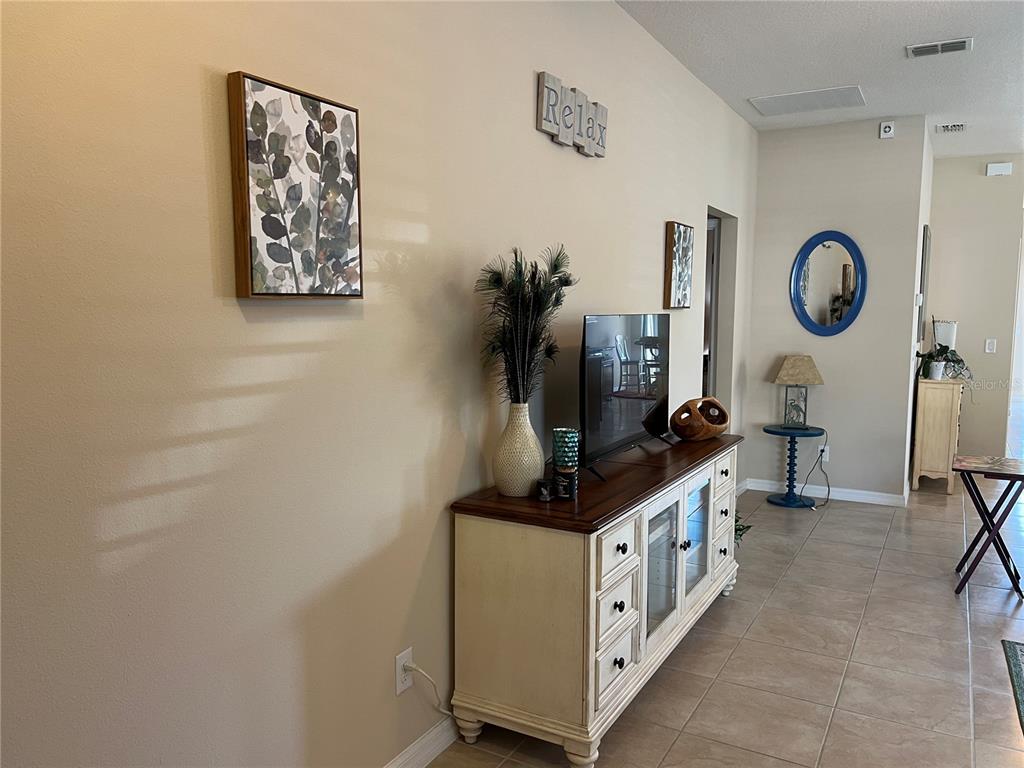 An open-concept living area features beige tile flooring, neutral walls, and a kitchen in the background — 2002 FISHTAIL FERN WAY, OCOEE, FL