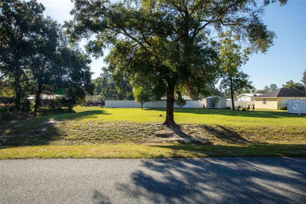 A grassy, tree-lined vacant lot is bordered by a white fence and a paved road — 618 SE 44TH STREET, KEYSTONE HEIGHTS, FL