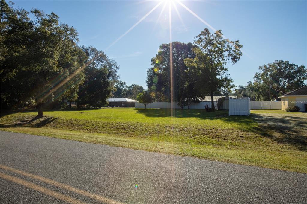A grassy vacant lot sits beside a paved road with trees and a white fence — 618 SE 44TH STREET, KEYSTONE HEIGHTS, FL
