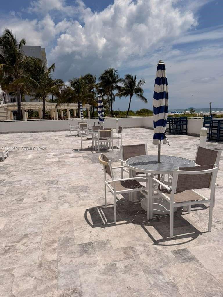 An outdoor patio features stone tile flooring, several dining tables with umbrellas, and palm trees — 401 Ocean Dr # 224, Miami Beach FL 33139, MIAMI BEACH, FL