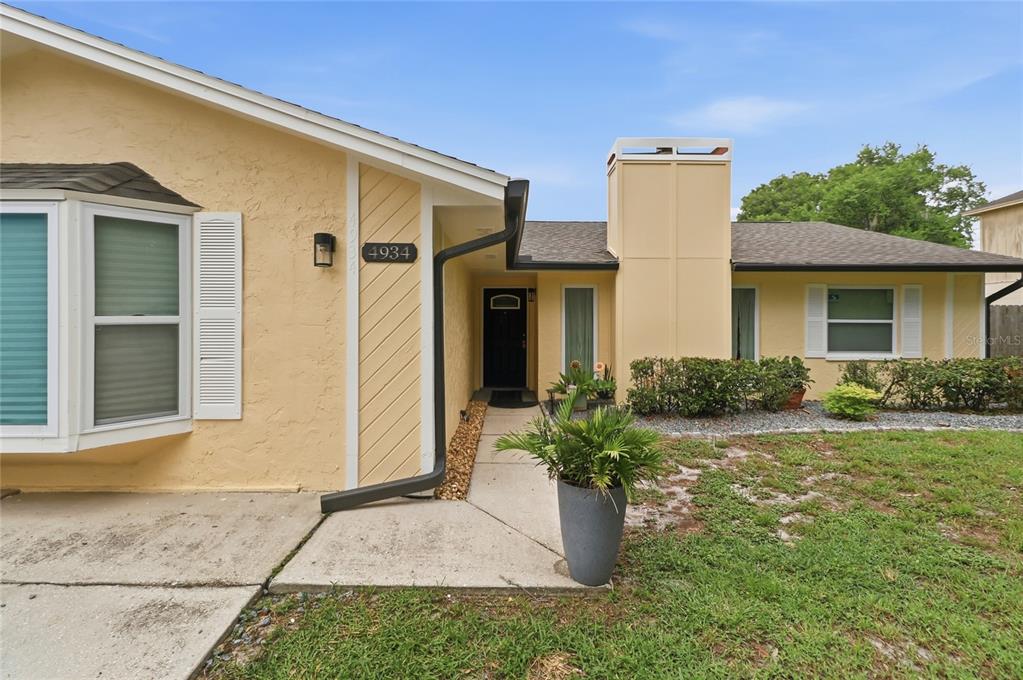 A yellow single-story house features a black front door, a chimney, and a bay window — 4934 WILDFLOWER DRIVE, LAKELAND, FL