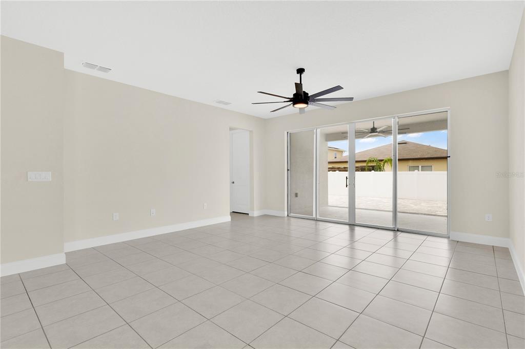 A spacious living room features light tile flooring, a ceiling fan, and sliding glass doors — 5631 WESTERN SUN DRIVE, ST CLOUD, FL