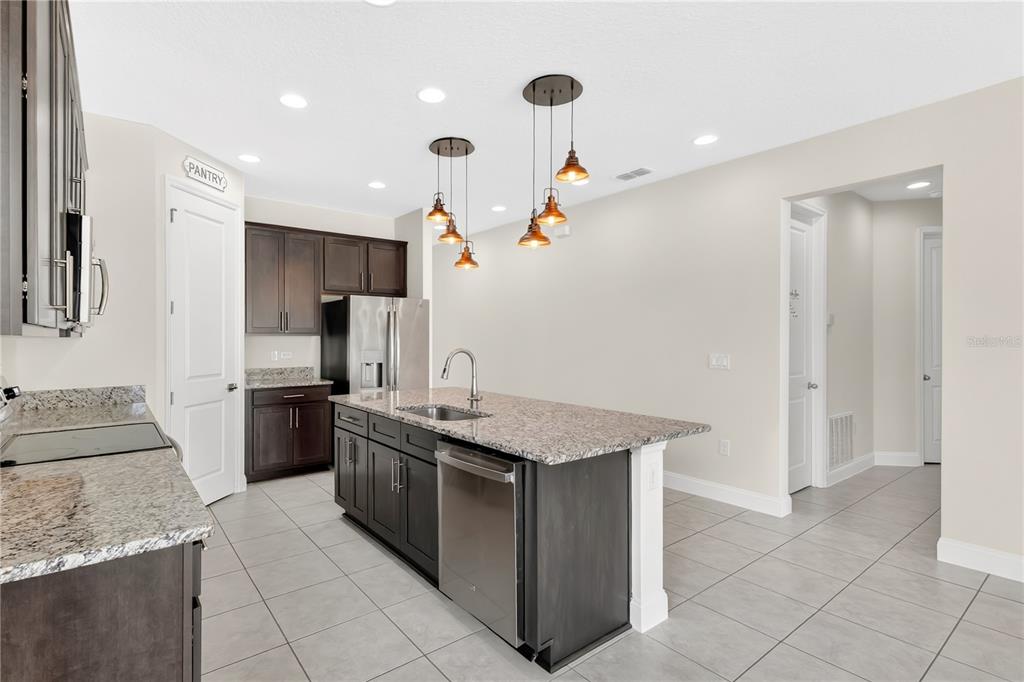 A kitchen features dark wood cabinets, granite countertops, a central island, and pendant lighting — 5631 WESTERN SUN DRIVE, ST CLOUD, FL