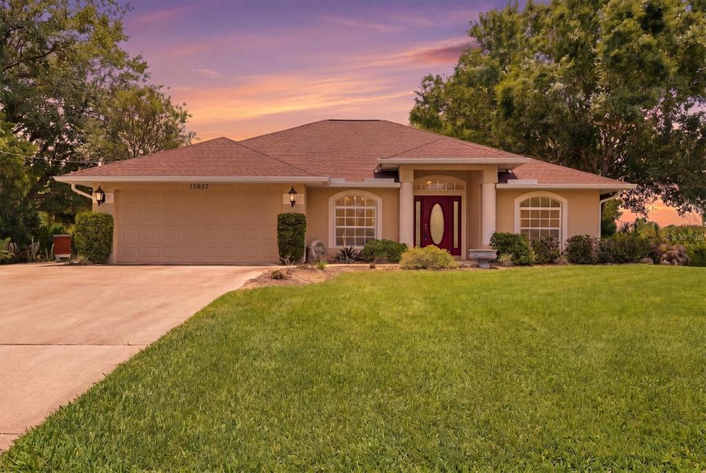 A single-story house with a tan stucco exterior, a two-car garage, and a red door — 12037 MALLORCA AVENUE, NORTH PORT, FL