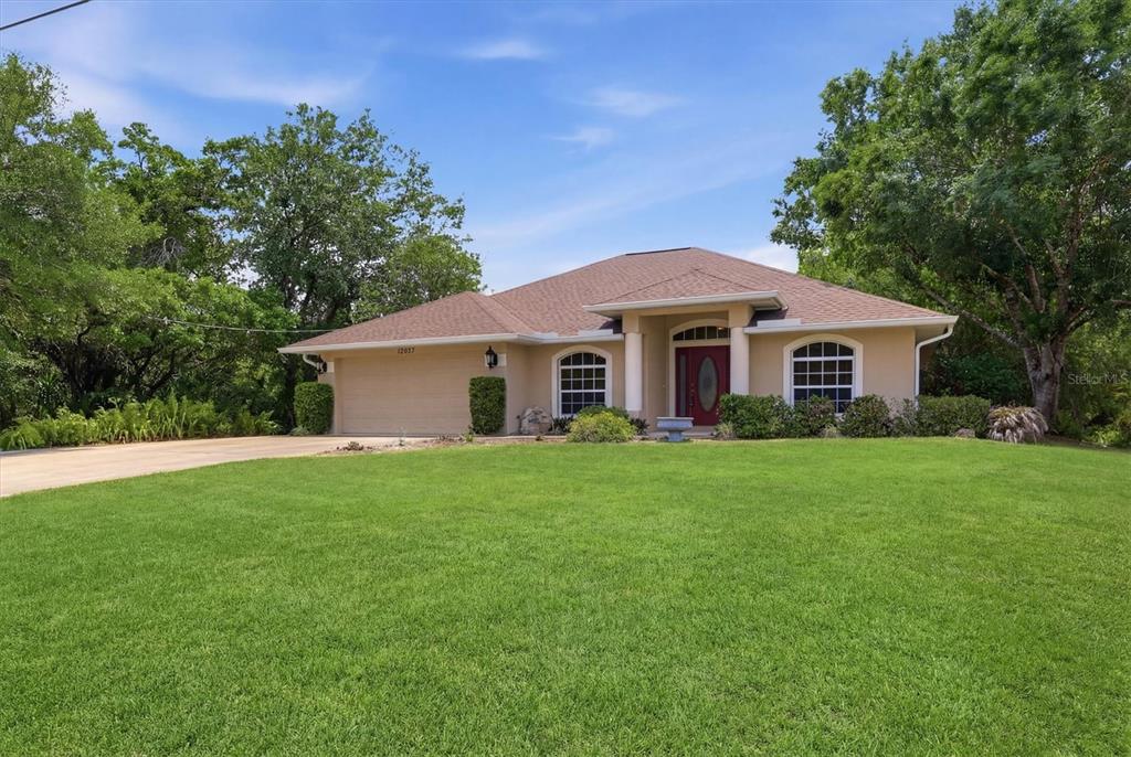 A single-story house with a tan exterior, a two-car garage, and a large front lawn — 12037 MALLORCA AVENUE, NORTH PORT, FL