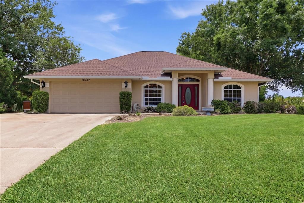 A single-story house with a tan stucco exterior, a red front door, and a driveway — 12037 MALLORCA AVENUE, NORTH PORT, FL