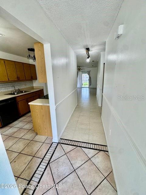 A hallway with tiled floors leads from a kitchen with wood cabinets toward a living area — 1220 CHENEY HIGHWAY UNIT D, TITUSVILLE, FL