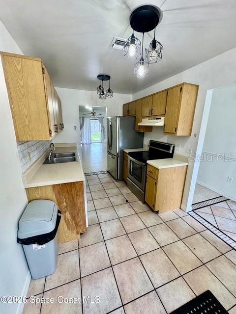 A kitchen features light wood cabinets, tile flooring, stainless steel appliances, and a pendant light — 1220 CHENEY HIGHWAY UNIT D, TITUSVILLE, FL