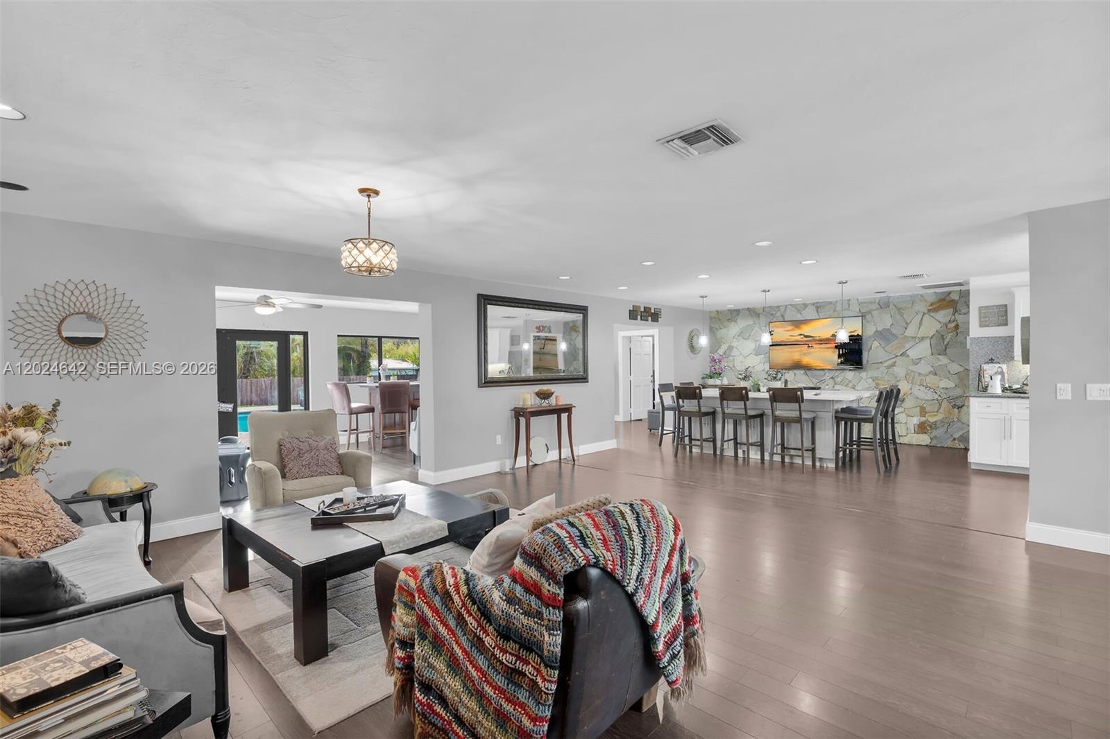 An open-concept living and dining area features a stone accent wall and hardwood floors — 8825 SW 185th Ter, Cutler Bay FL 33157, CUTLER BAY, FL