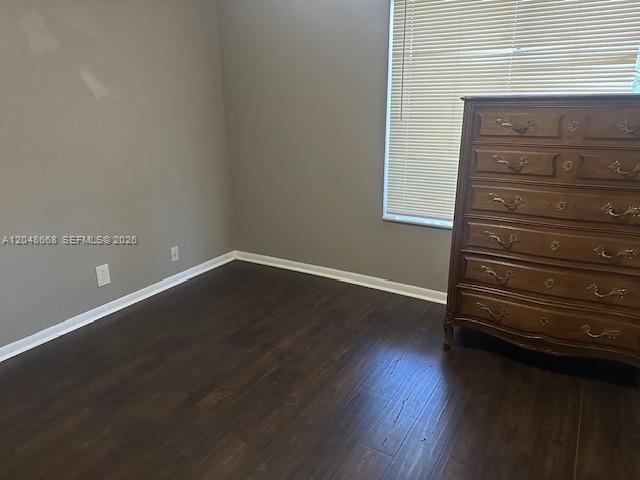 A bedroom with dark wood flooring, gray walls, and a wooden dresser near a window — 5252 Bosque Ln # 9, West Palm Beach FL 33415, WEST PALM BEACH, FL