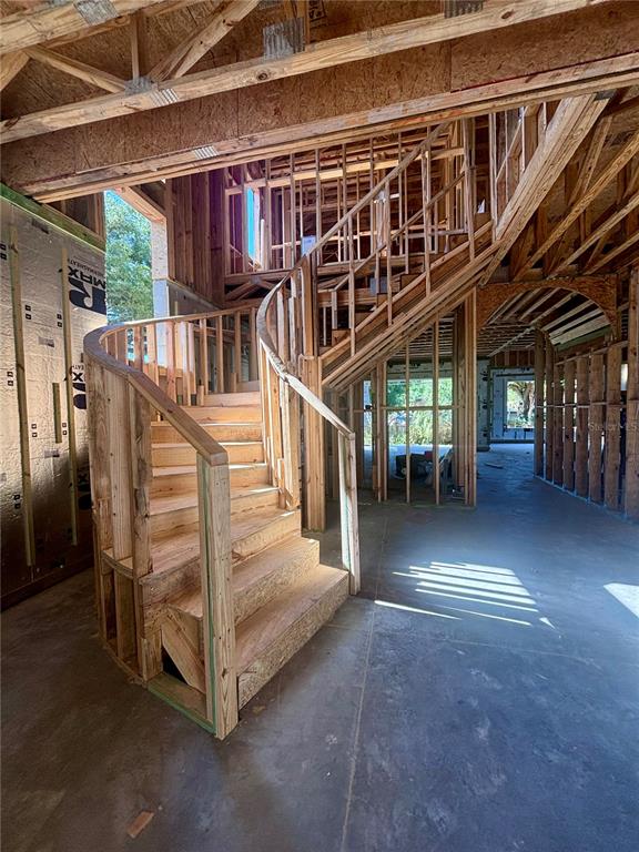A wooden curved staircase under construction stands in an unfinished room with exposed wall studs — 4414 W LAWN AVENUE, TAMPA, FL