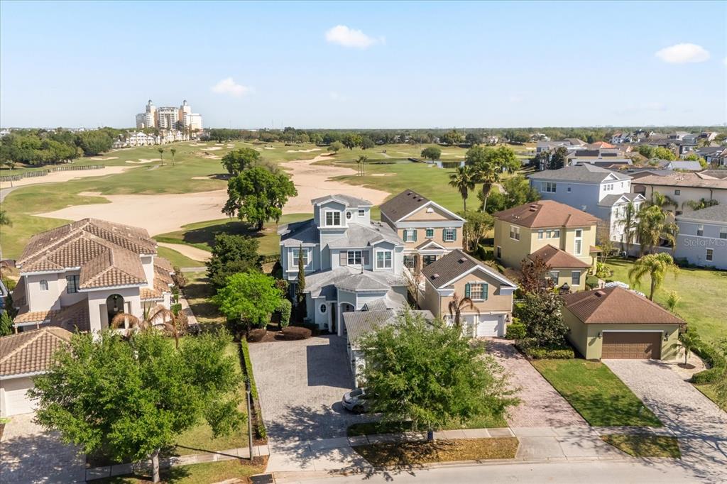 An aerial view shows a multi-story house with a paved driveway next to a golf course — 7447 EXCITEMENT DRIVE, REUNION, FL