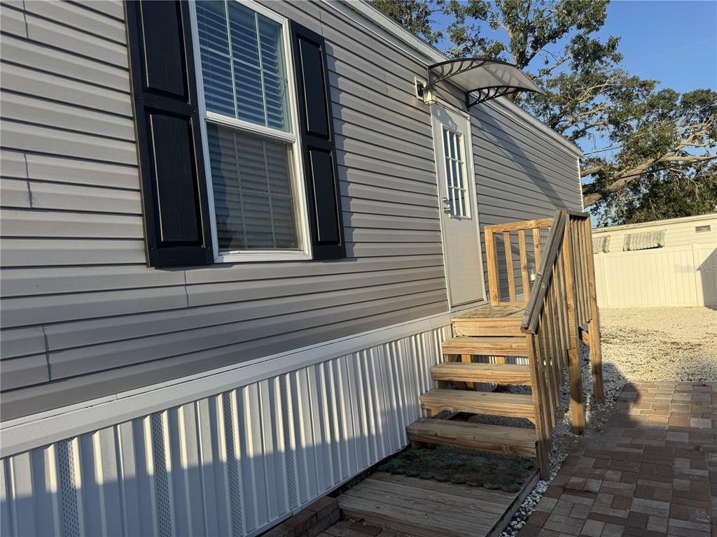 A side view of a manufactured home with gray siding, black shutters, and wooden stairs — 2013 KEPNER DRIVE, HOLIDAY, FL