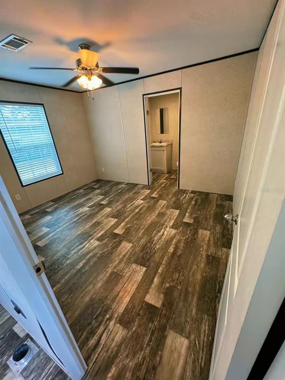 A bedroom features wood-look flooring, a ceiling fan, and an open doorway to a bathroom — 2013 KEPNER DRIVE, HOLIDAY, FL
