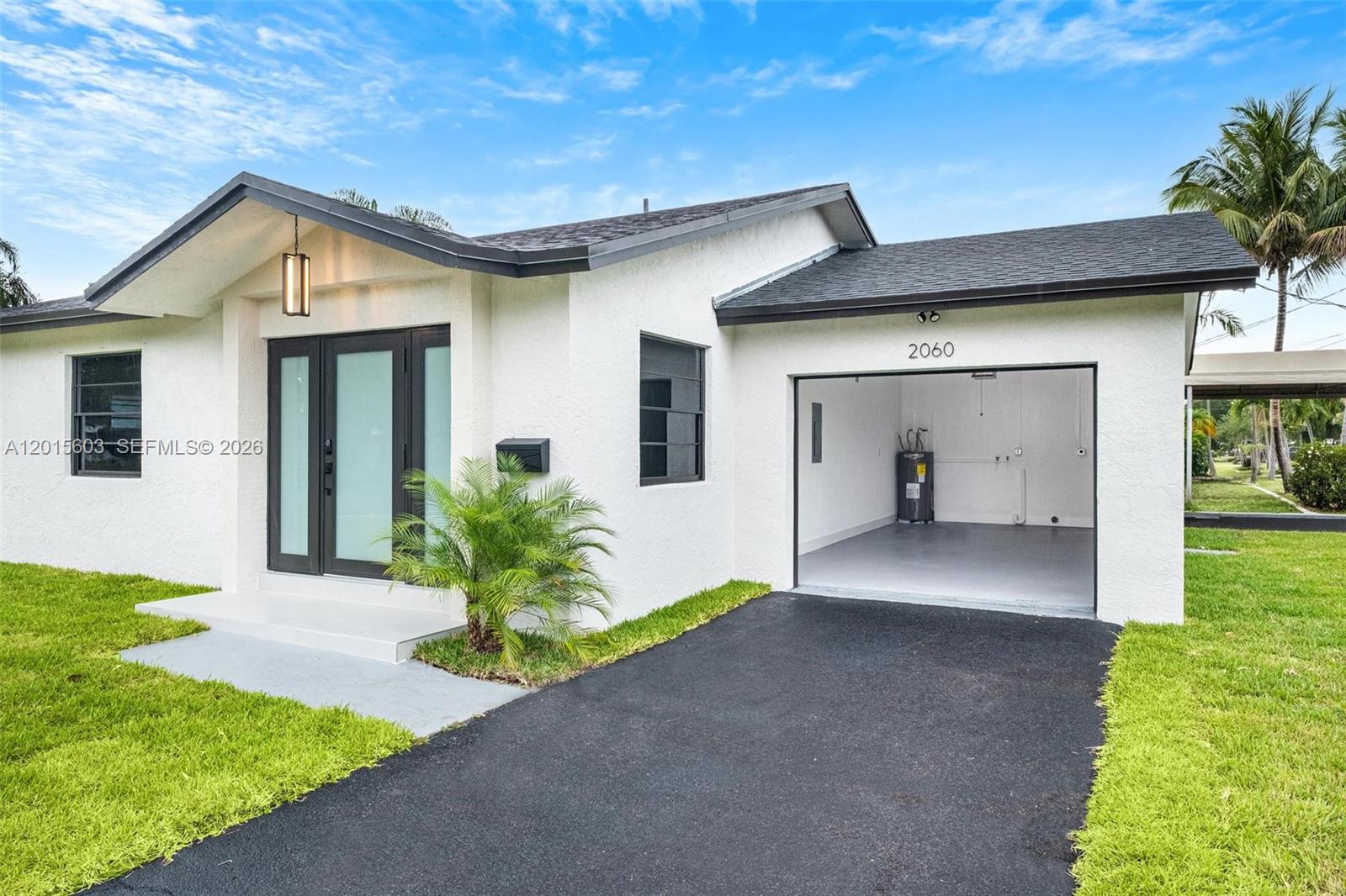 A white single-story house features a black-framed front door, a garage, and a paved driveway — 2060 N 26th Ave, Hollywood FL 33020, HOLLYWOOD, FL