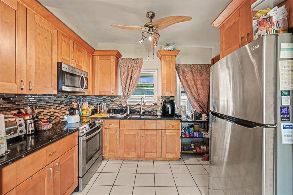 A kitchen features wood cabinets, stainless steel appliances, a tiled backsplash, and white floor tiles — 1431 HESTER DRIVE, LAKELAND, FL