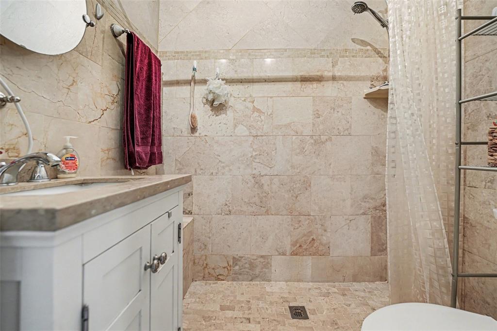 A bathroom features a white vanity, a walk-in shower with beige stone tile, and a showerhead — 1431 HESTER DRIVE, LAKELAND, FL
