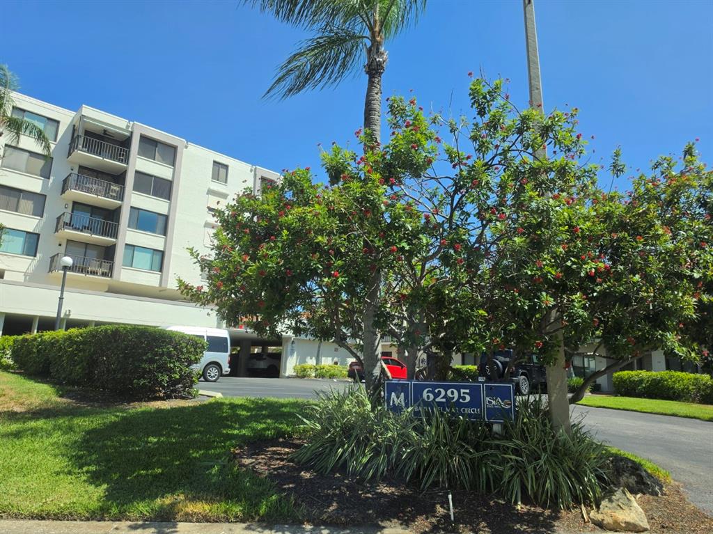 A multi-story apartment building stands behind a landscaped lawn with a prominent address sign — 6295 BAHIA DEL MAR CIRCLE UNIT 111, ST PETERSBURG, FL