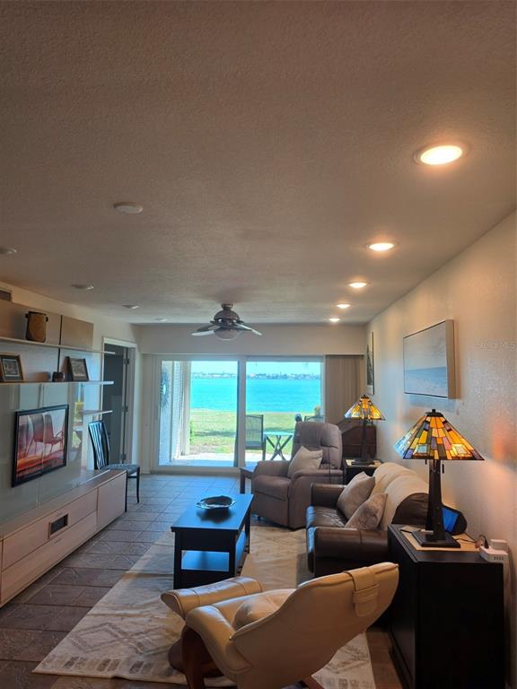 A living room features a television, seating, and a sliding glass door overlooking the water — 6295 BAHIA DEL MAR CIRCLE UNIT 111, ST PETERSBURG, FL