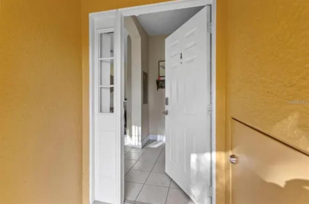 An open white front door leads into a tiled entryway with a side window panel — 8416 BLUE LAGOON DRIVE, KISSIMMEE, FL