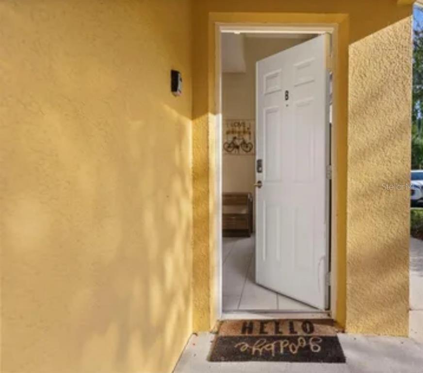 A yellow exterior wall features an open white door leading into a tiled entryway — 8416 BLUE LAGOON DRIVE, KISSIMMEE, FL