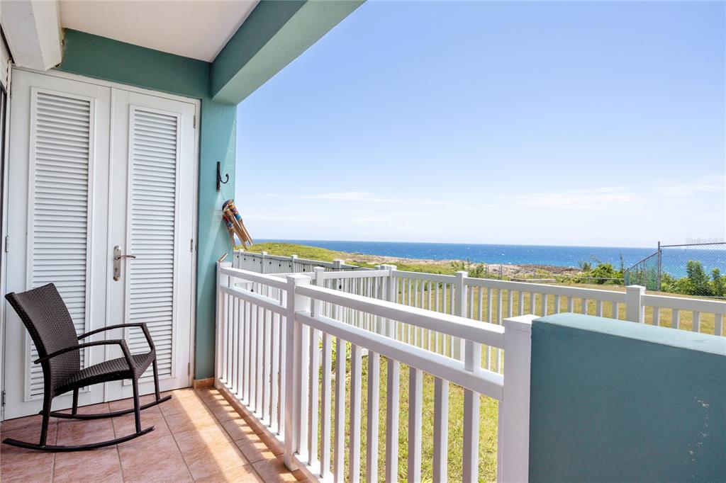 A balcony with a rocking chair overlooks a grassy yard and the ocean — 5 LOLITA NATAL UNIT 502, MANATI, PR