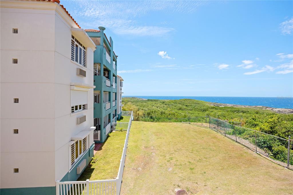 An exterior view of a multi-story apartment building overlooking a grassy yard and the ocean — 5 LOLITA NATAL UNIT 502, MANATI, PR