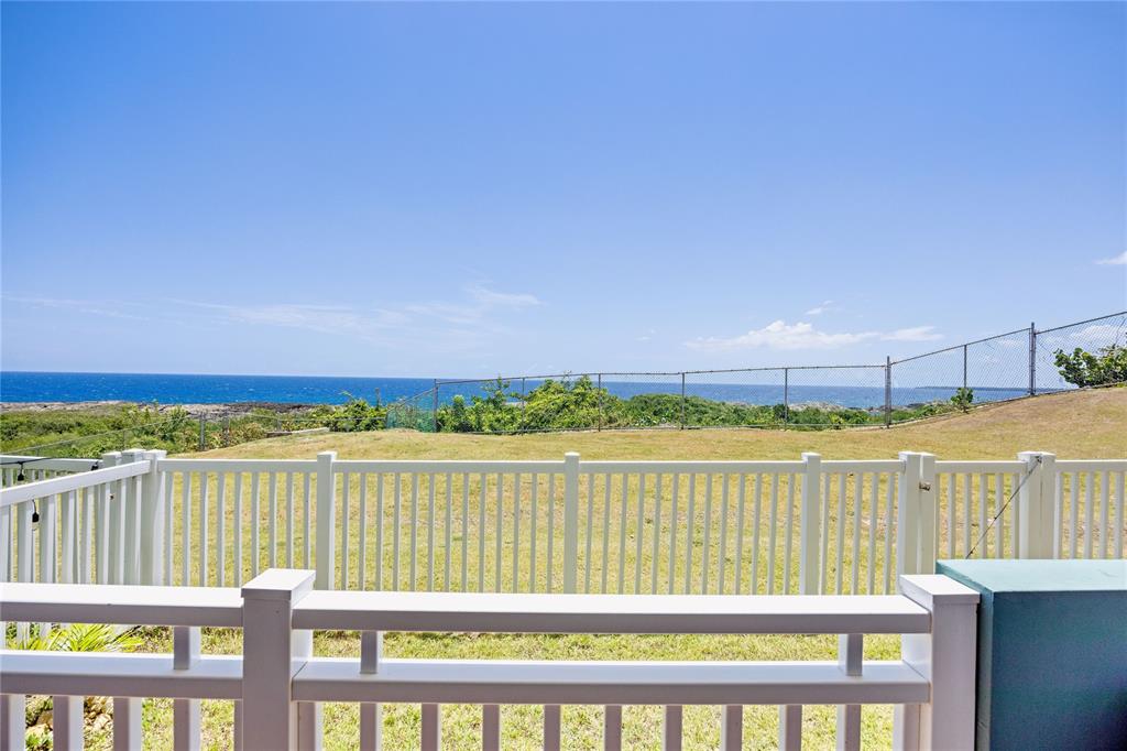 A white vinyl railing overlooks a grassy yard with a chain-link fence and ocean view — 5 LOLITA NATAL UNIT 502, MANATI, PR