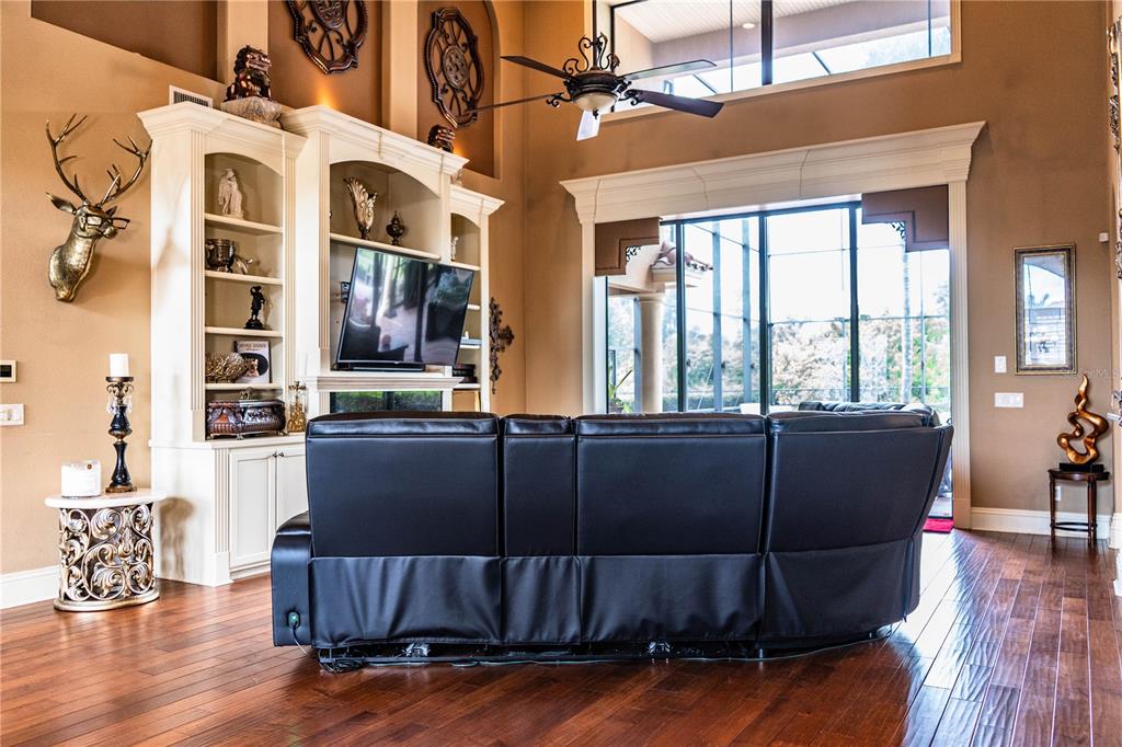 A living room features a black leather sectional, built-in shelving, and large windows — 6739 EAGLE RIDGE BOULEVARD, LAKELAND, FL