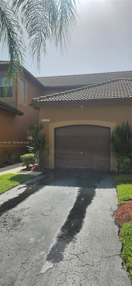 A brown stucco house features a single-car garage and a cracked asphalt driveway — 1599 Veracruz Ln, Weston FL 33327, WESTON, FL