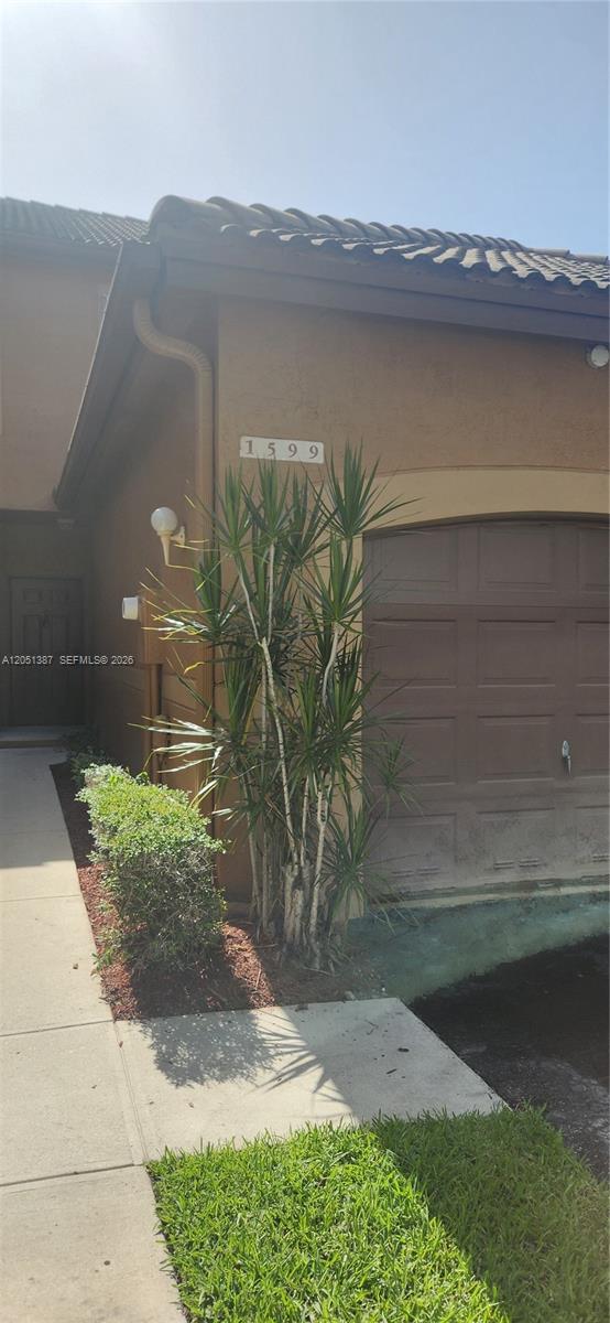 A tan exterior wall features a house number, a garage door, and a tall plant — 1599 Veracruz Ln, Weston FL 33327, WESTON, FL