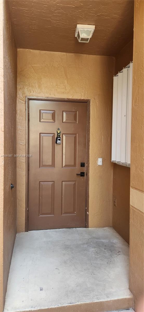 A brown front door with a lockbox is situated in a recessed concrete entryway — 1599 Veracruz Ln, Weston FL 33327, WESTON, FL