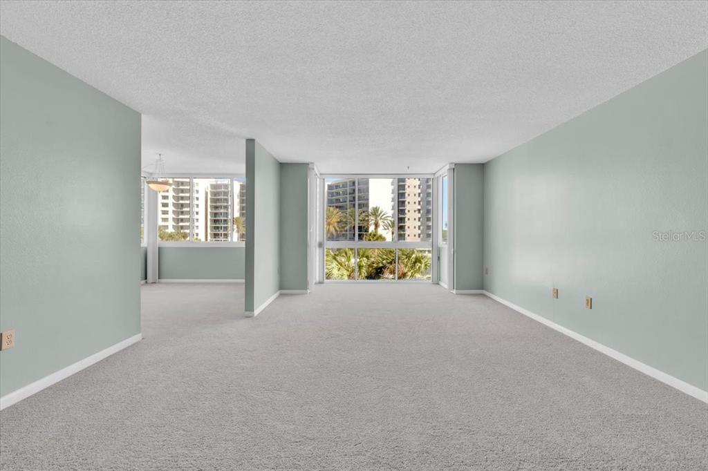An empty living room with light gray walls, beige carpeting, and large floor-to-ceiling windows — 660 ISLAND WAY UNIT 301, CLEARWATER BEACH, FL