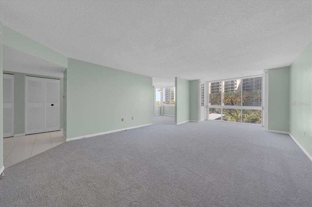 A spacious living area features light green walls, gray carpeting, and large windows with palm trees — 660 ISLAND WAY UNIT 301, CLEARWATER BEACH, FL