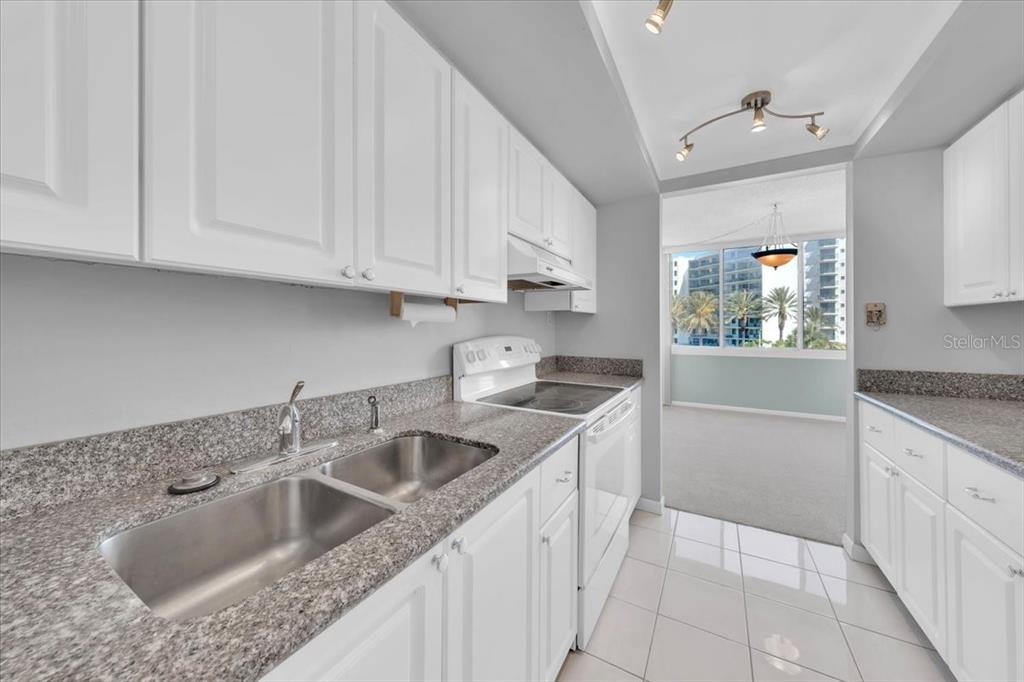 A kitchen with white cabinets, granite countertops, and a view of a balcony outside — 660 ISLAND WAY UNIT 301, CLEARWATER BEACH, FL