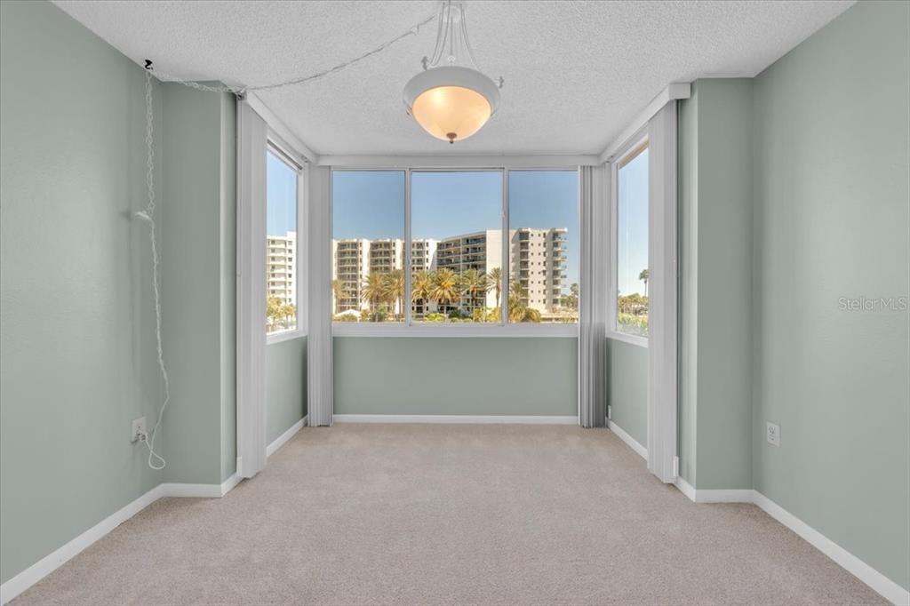 A sunroom with light green walls, beige carpeting, a central pendant light, and large windows — 660 ISLAND WAY UNIT 301, CLEARWATER BEACH, FL