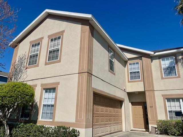 A two-story beige stucco townhouse features a garage and multiple windows under a clear sky — 439 BLOOMINGDALE DRIVE, DAVENPORT, FL